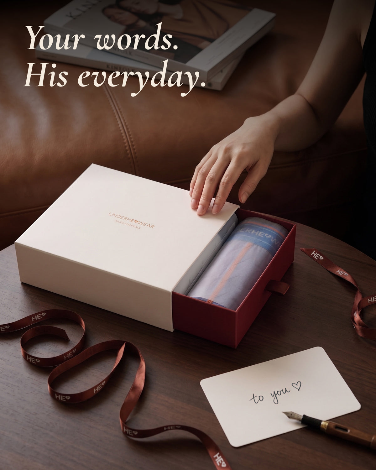 A hand opening an underherwear gift box with lavender boxer briefs, ribbon and a handwritten note.