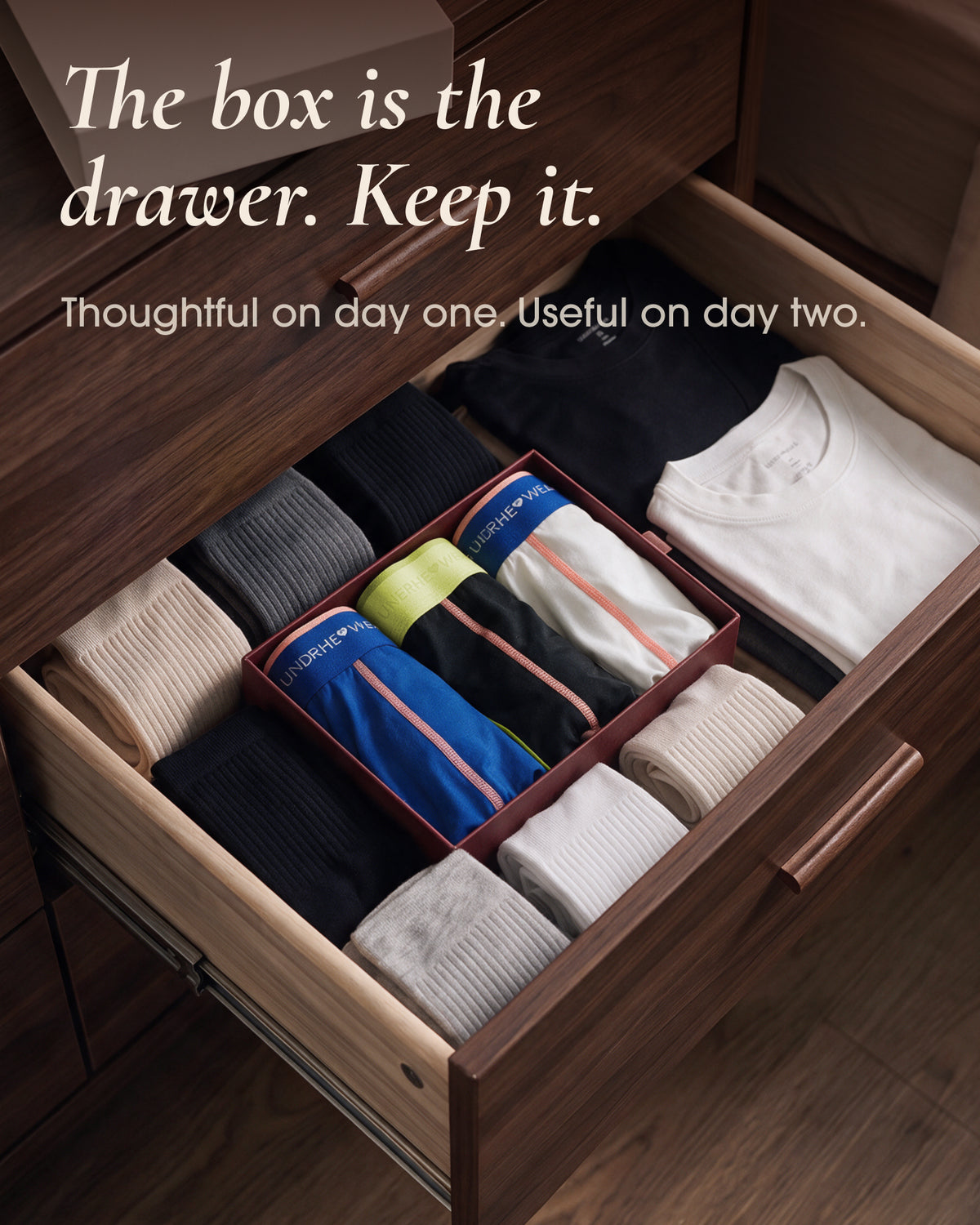 An underherwear gift box holding rolled underwear inside a wooden drawer beside folded socks and shirts.